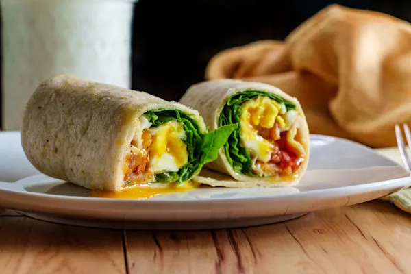 Flavorful Veggie Breakfast Wrap, packed with fluffy scrambled eggs, organic spinach, savory portobello mushrooms, fresh feta cheese, crispy hash browns, house-made aioli, and a touch of maple syrup, all wrapped in a warm flour tortilla.