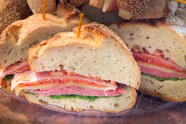 Each half sandwich is loaded with savory ham, bold salami, rich mortadella, and creamy provolone cheese, complemented by juicy sliced tomatoes, crisp red onions, peppery baby organic arugula, and zesty banana peppers. Finished with a spread of mayo, mustard, and a drizzle of our signature house-made Italian dressing, all nestled in a freshly baked hoagie roll.