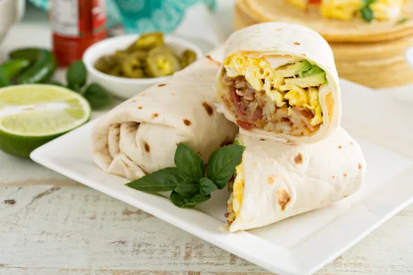 A bold mix of fluffy scrambled eggs, crispy thick-cut bacon, American yellow cheddar cheese, spicy jalapeños, freshly sliced avocado, smoky chipotle sauce, crispy hash browns, and a hint of maple syrup, all wrapped in a warm flour tortilla.